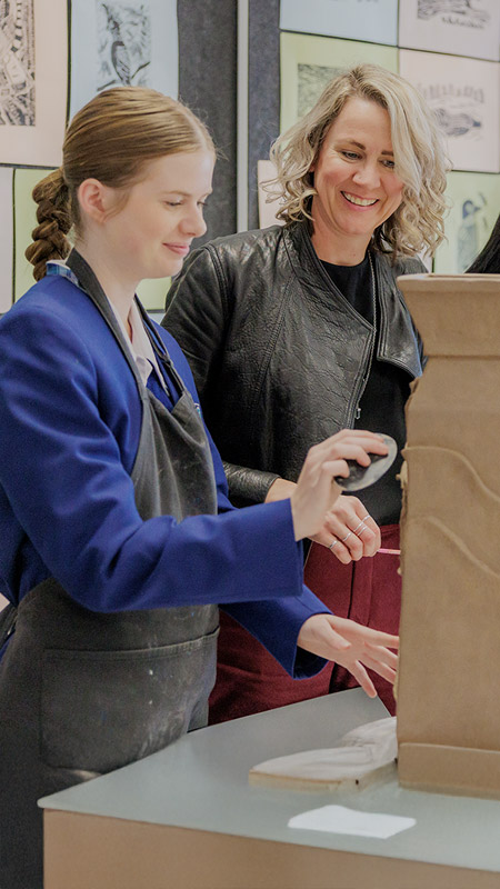 Caroline Chisholm Catholic College Glenmore Park teacher assisting students in art class. The students are sculpting