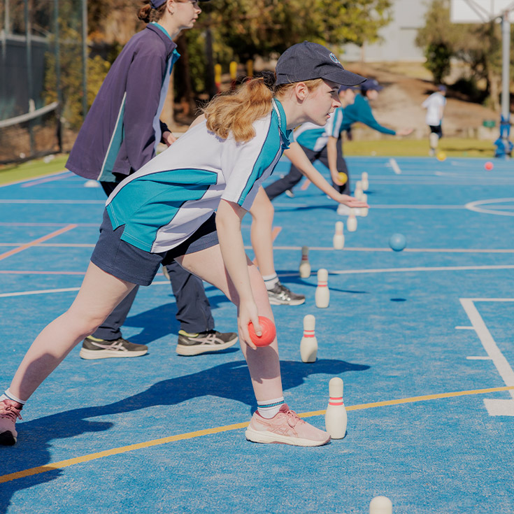 Caroline Chisholm Catholic College Glenmore Park student playing bowls on an outdoor basketball court